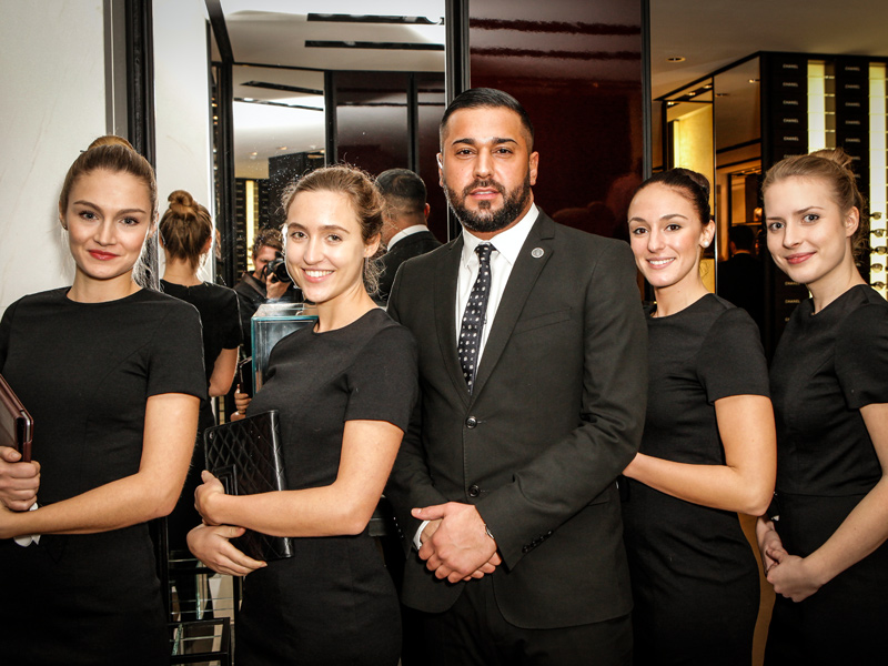 Vier Hostessen in schicken schwarzen Kleidern mit einem Mann im Anzug in der Mitte, eleganter Auftritt bei Event, Gala und Empfangsservice