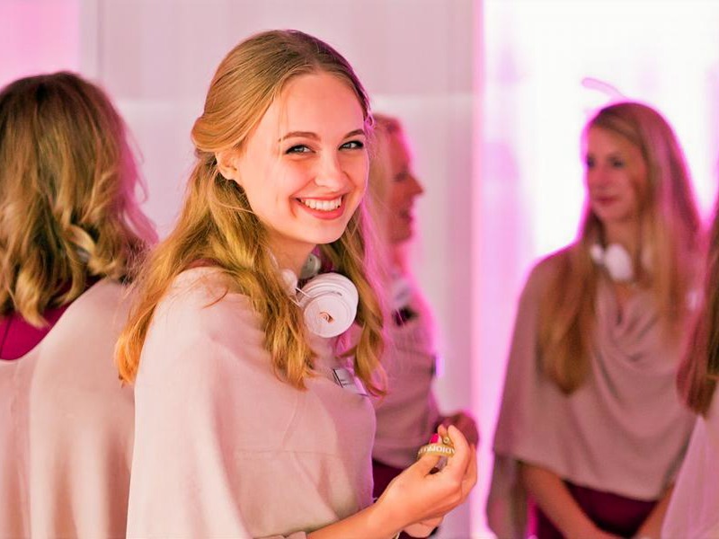 Mehrere Hostessen in einheitlichen Outfits mit wei&szlig;en Kopfh&ouml;rern um den Hals, eine l&auml;chelt in die Kamera bei einem Promotion Event