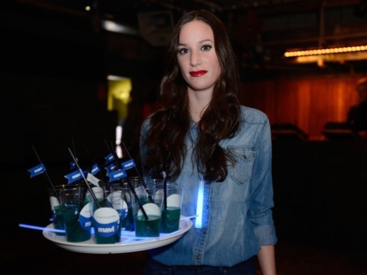 Freundliche Hostess im Jeanshemd mit Tablet und Getränk in der Hand, roter Lippenstift, professioneller Service bei Event und Promotion