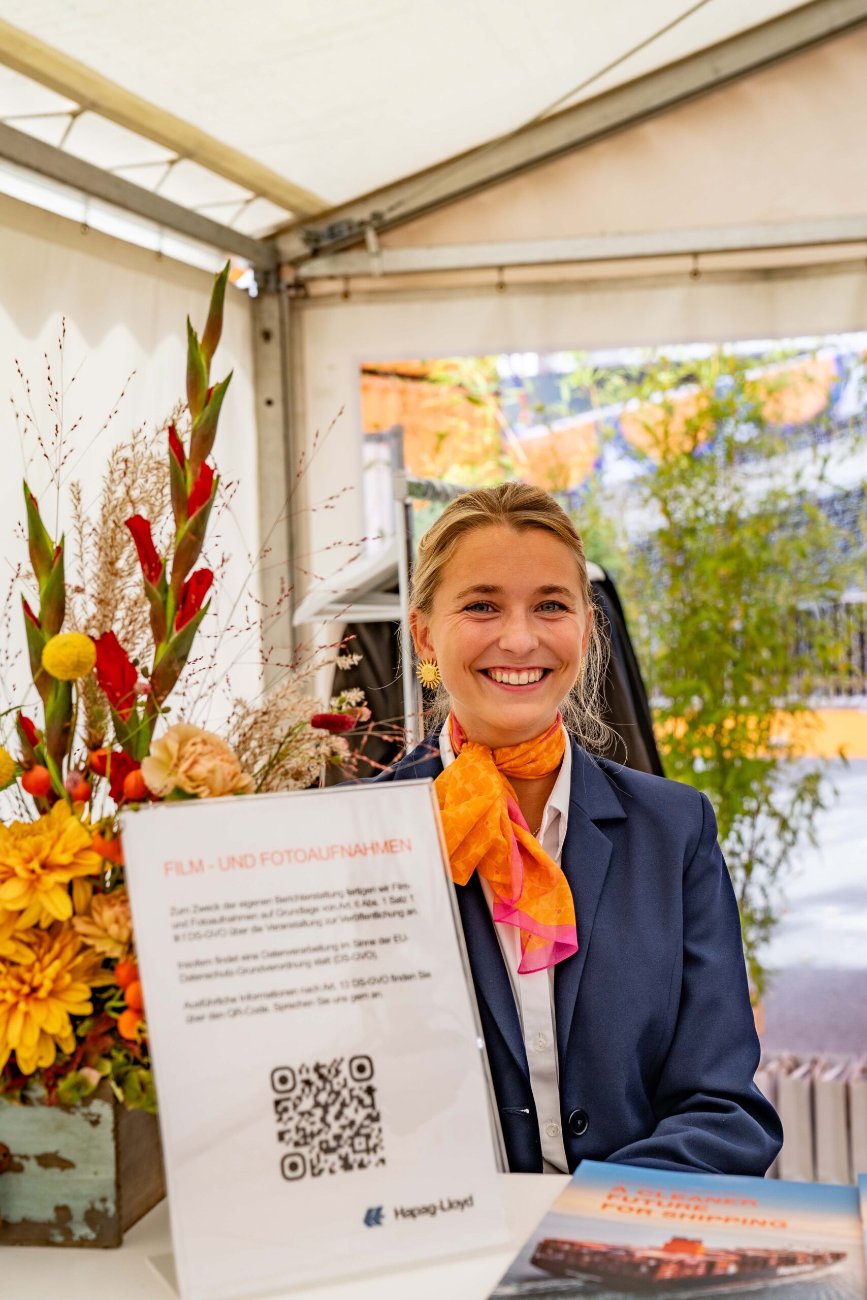 Hostess im blauen Hosenanzug mit orangem Halstuch arbeitet an der Garderobe, lächelnder Empfangsservice bei Event, Gala und Veranstaltung