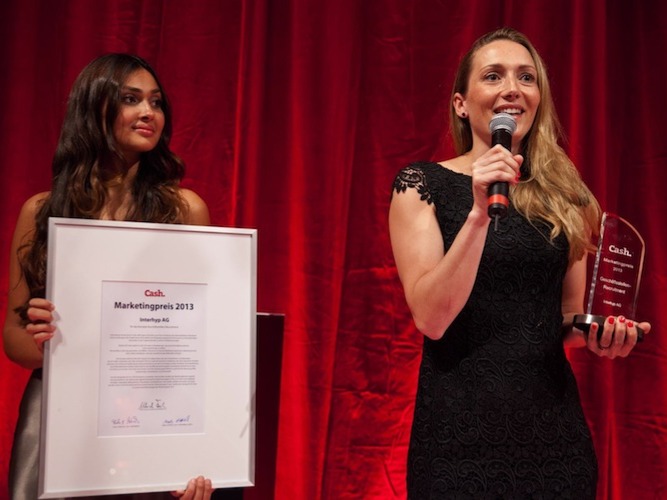 Eventhostess als Moderatorin im schwarzen Kleid mit Mikrofon und Preis, im Hintergrund Kollegin mit Urkunde, professionelle Moderation bei Gala und Event