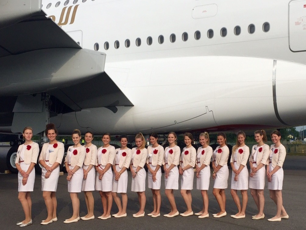Hostessen in weißen Kostümen mit rotem Hemd stehen vor einem Flugzeug in einer Reihe, lächelnder Promotion Einsatz bei Event und Flughafenaktion