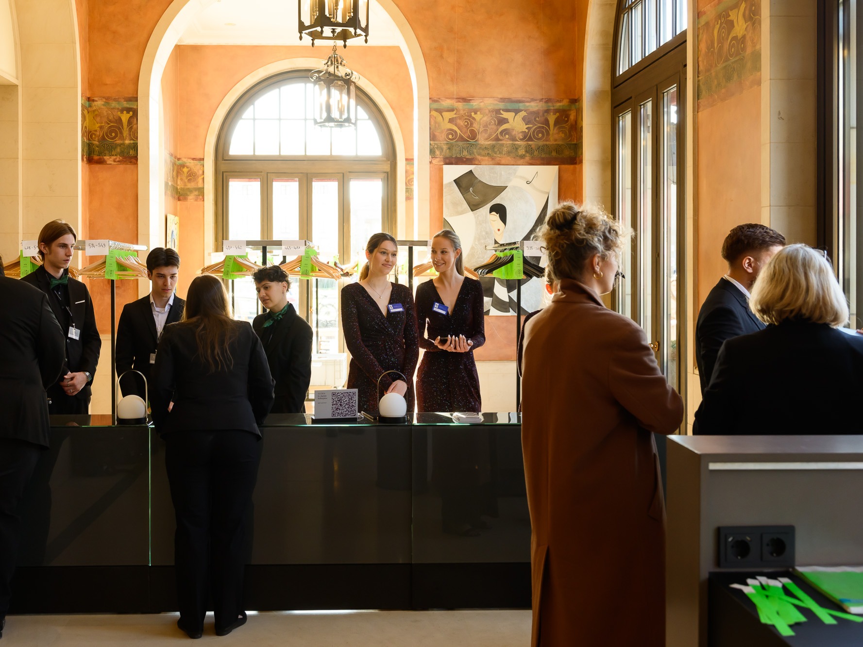 Hostessen und Hosts stehen hinter einem kniehohen Tresen bei einer Tagung, elegant gekleidet in Abendkleidern und Anzügen, professioneller Empfang bei Event
