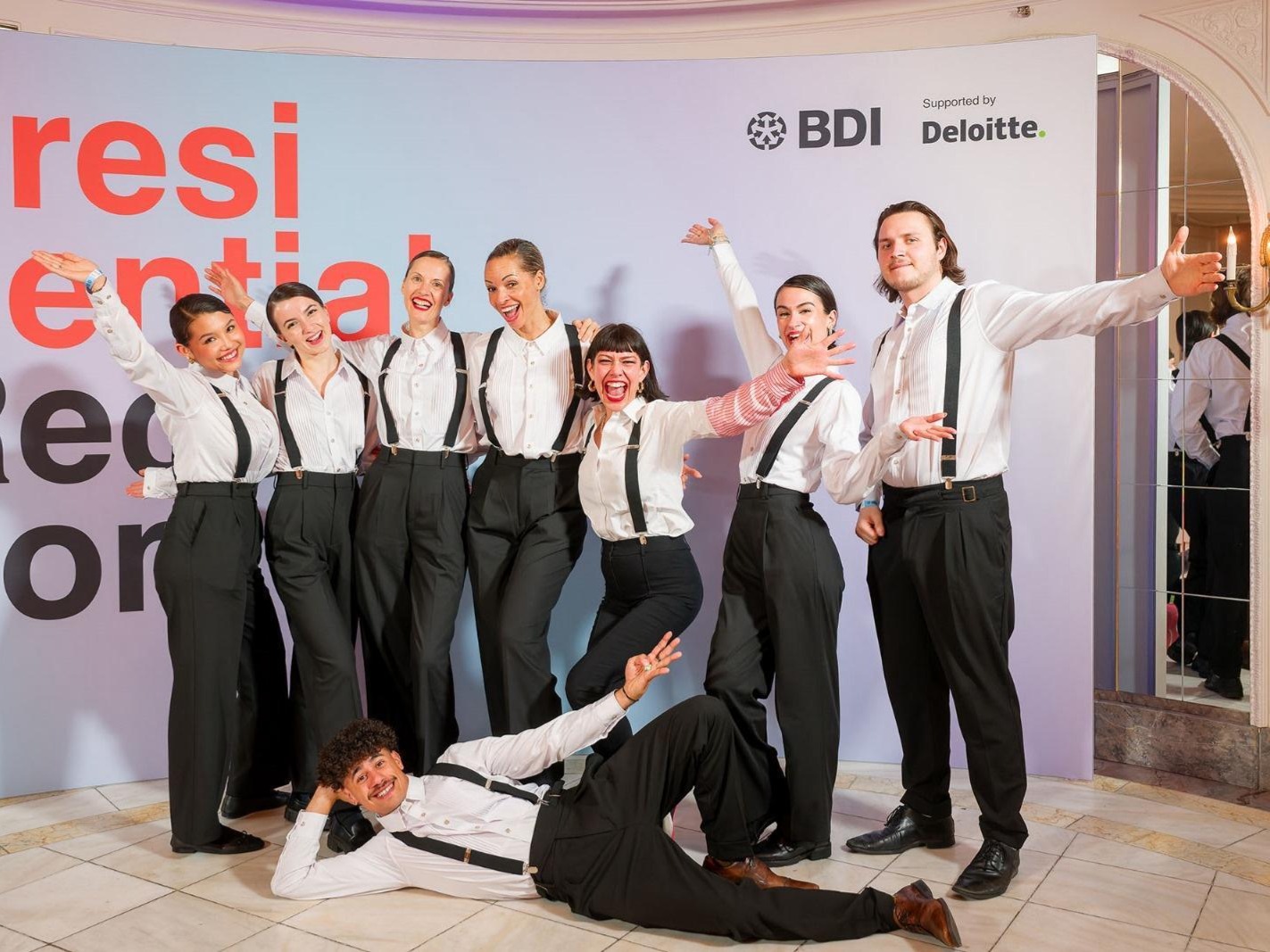 Acht Hosts und Hostessen in schwarzen Hosen, weißen Hemden und Hosenträgern jubeln vor einem Aufsteller, gute Stimmung bei Event und Promotion Einsatz