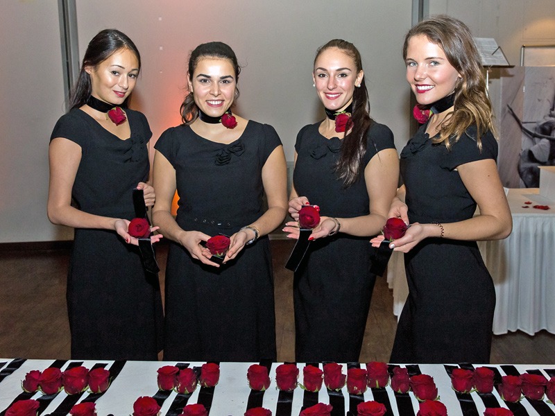 Vier Hostessen in eleganten schwarzen Kleidern an der Akkreditierung, rote Armbänder auf einem Tisch, professioneller Check-in bei Event und Veranstaltung