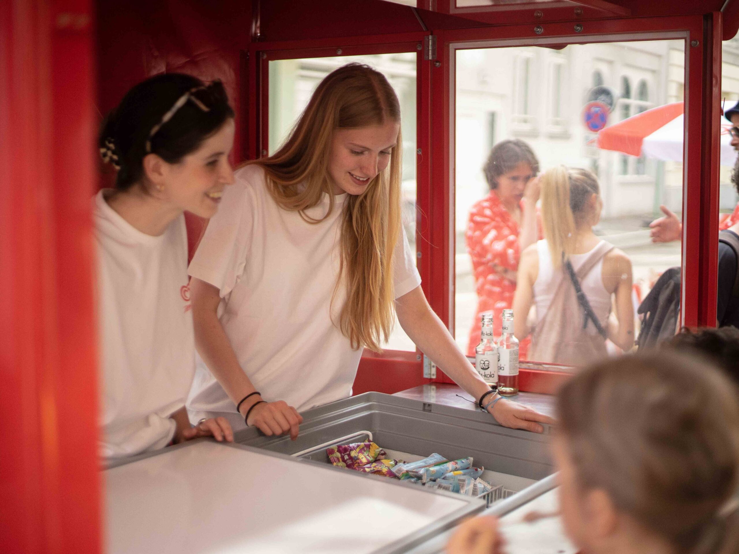 Zwei Promotion Hostessen in weißen T-Shirts betreuen einen Stand und verteilen Eis, sommerliche Markenaktion bei Event und Promotion Einsatz