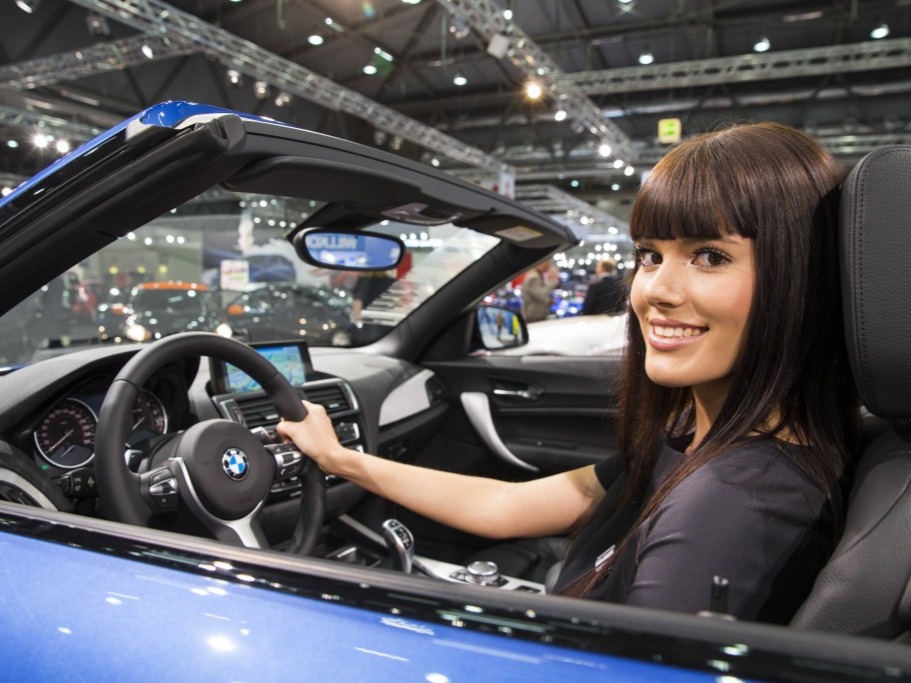 Lächelnde Hostess sitzt in einem ausgestellten Auto auf einer Messe, freundliche Ausstrahlung bei Promotion, Event und Markenpräsentation