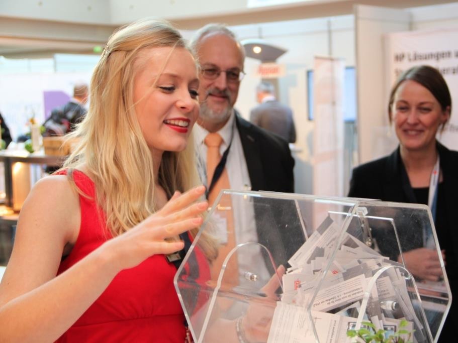 Hostess im roten Kleid mit rotem Lippenstift betreut eine Losbox, Promotion Aktion bei Event, Gewinnspiel und Markenaktivierung