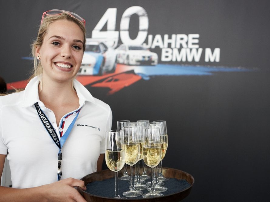 Lächelnde Hostess bei BMW 40 Jahre Feier mit Tablet und Sektgläsern, professioneller Getränkeservice bei Event und Markenveranstaltung