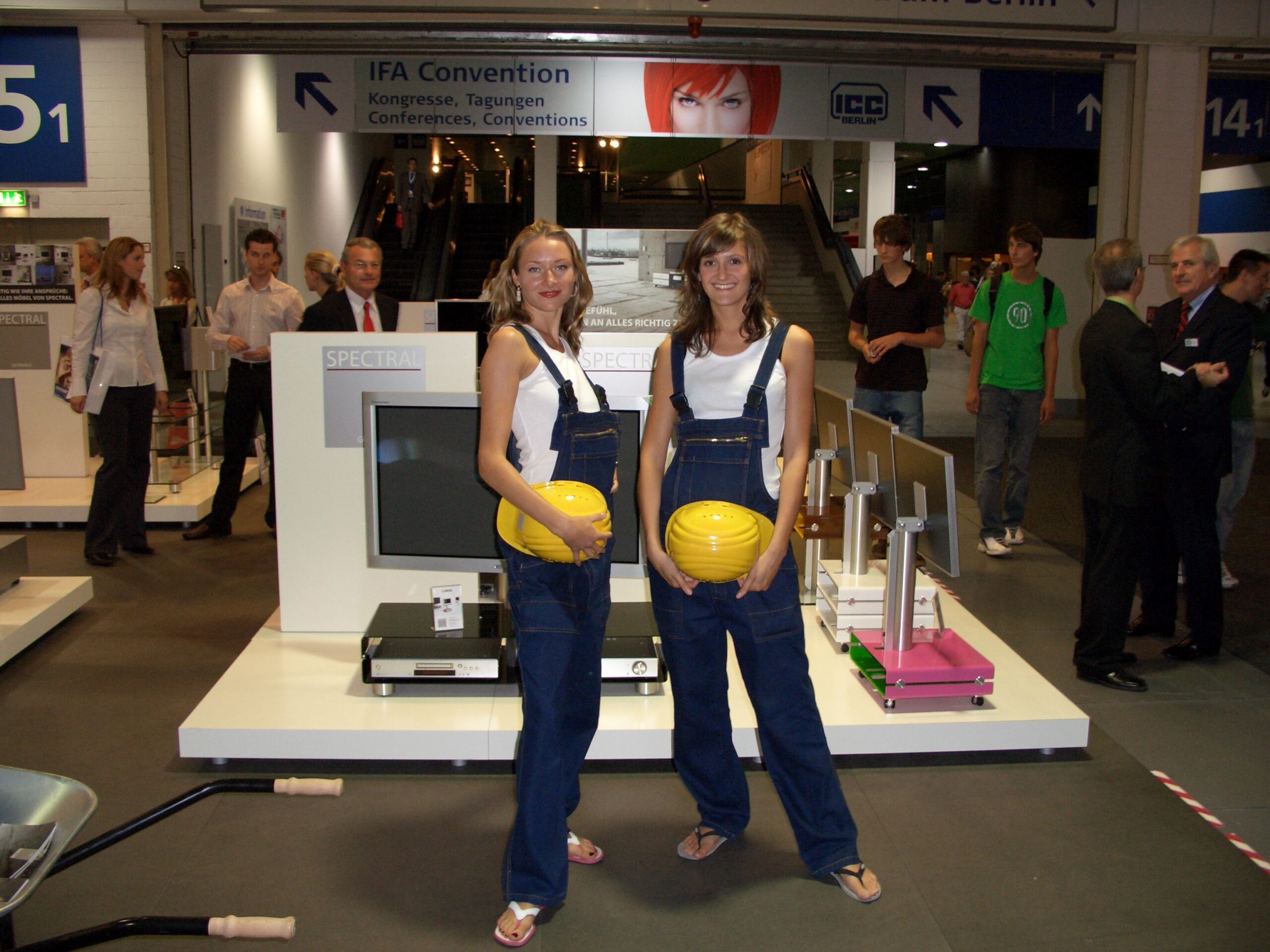 Zwei Frauen in Jeans-Overalls mit weißen Tops halten einen gelben Helm, Promotion Team im Einsatz bei Event, Messe und Markenaktivierung