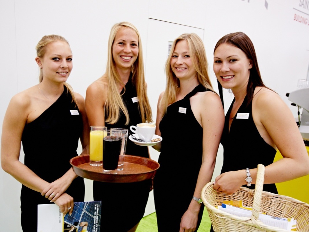 Vier Hostessen in schwarzen schulterfreien Kleidern im Catering, eine mit Tablet und Getränken, eine mit Kaffeetasse, professioneller Service bei Event
