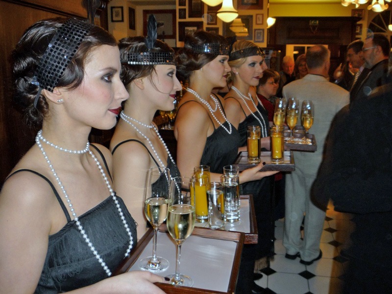 Hostessen in 80er-Jahre Kleidung mit Tablets und Getränken in der Hand, stilvolle Promotion bei Event, Messe und Themenveranstaltung
