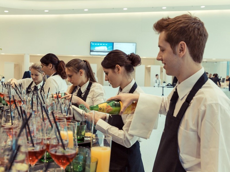 Hosts und Hostessen in Hemden und Schürzen schenken Getränke aus, professioneller Service bei Event, Messe und Gastronomie Einsatz