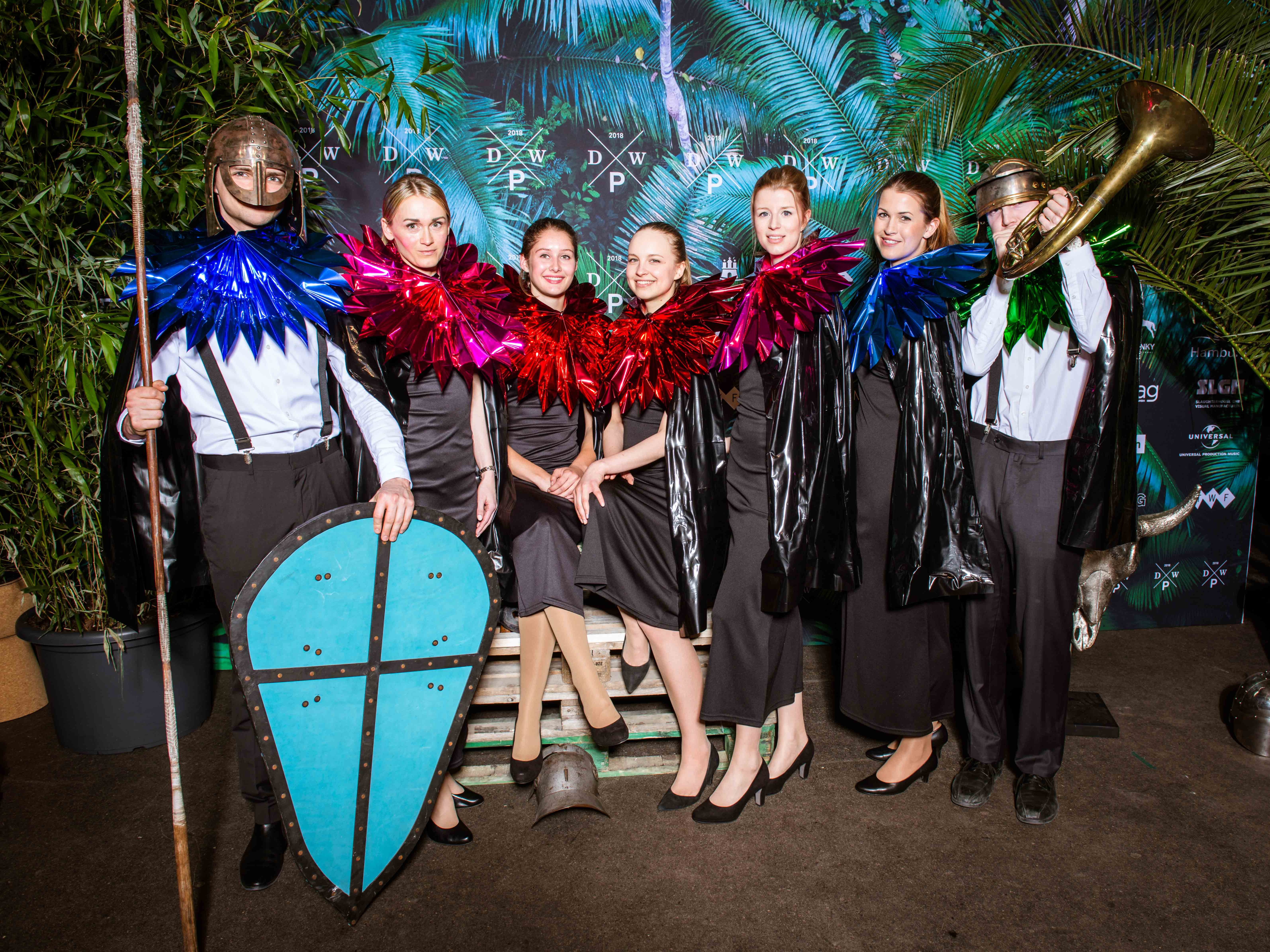 Sieben Hostessen und Hosts in schwarzen Kostümen mit auffälligen pinken Halskrausen auf dem roten Teppich, kreative Themen-Promotion mit mittelalterlicher Inszenierung