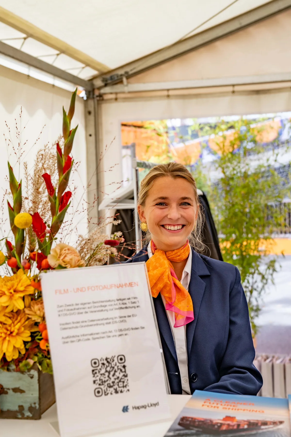 Hostess im blauen Hosenanzug mit orangem Halstuch arbeitet an der Garderobe, lächelnder Empfangsservice bei Event, Gala und Veranstaltung