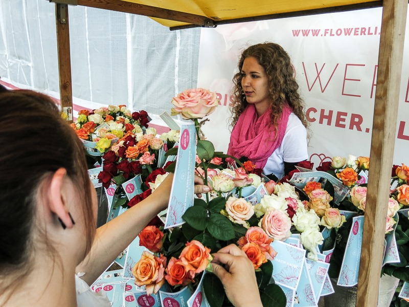 Promotion Hostess in weißem T-Shirt verteilt Blumen an Passanten, aufmerksamkeitsstarke Markenaktion bei Event, Messe und Straßenpromotion