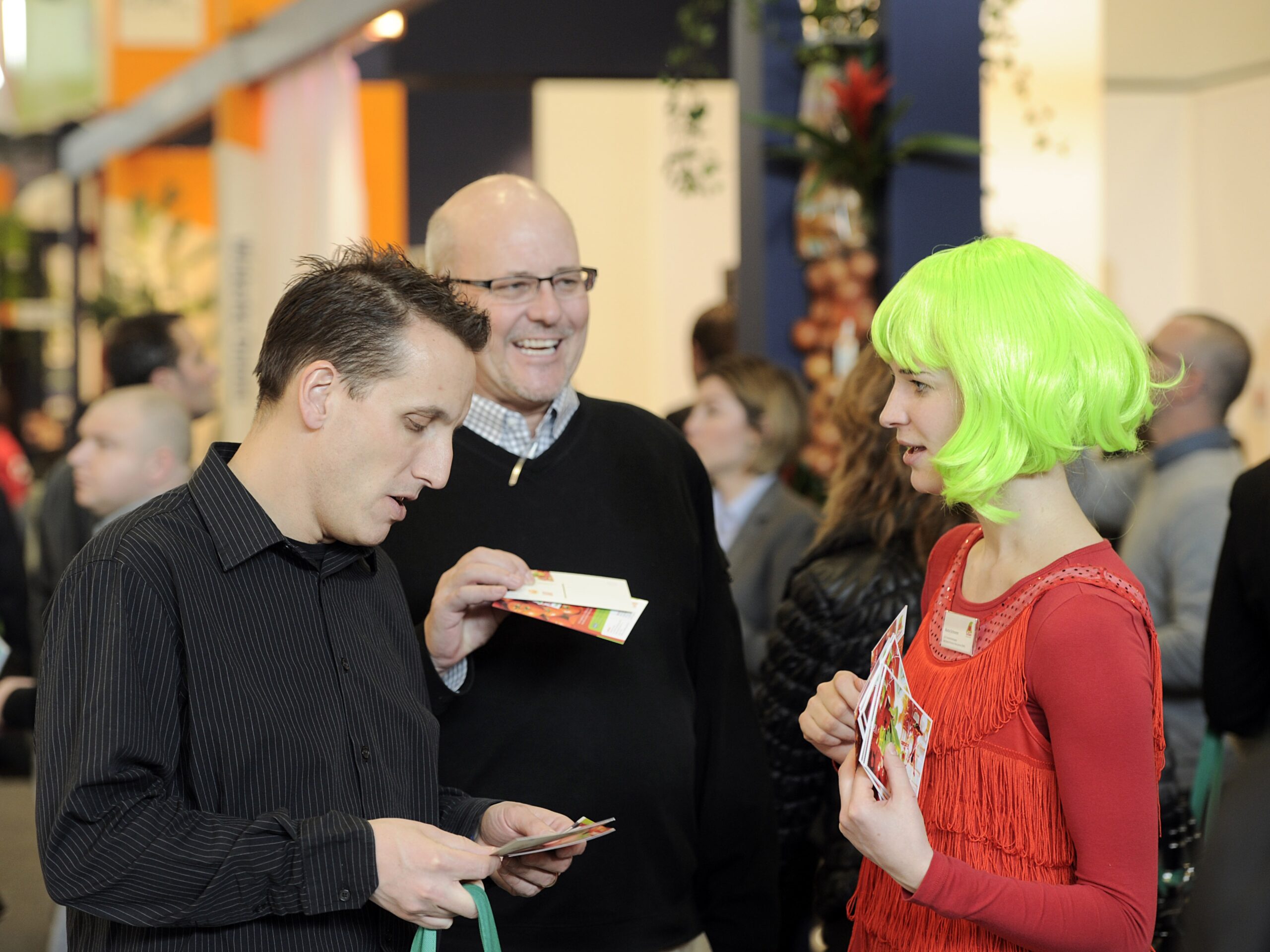 Promotion Hostess mit grüner Perücke und roter Kleidung verteilt Flyer an Passanten, auffällige Straßenpromotion bei Event und Markenaktion
