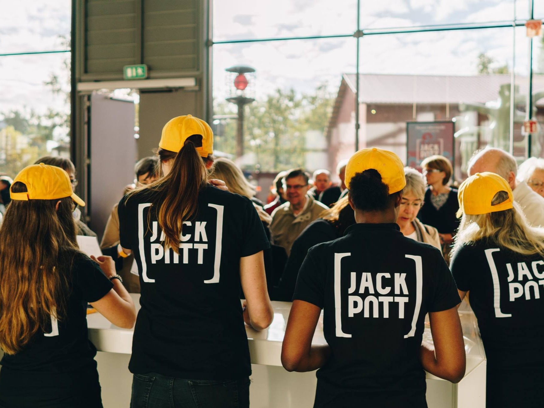 Vier Aufbauhelferinnen mit gelben Helmen und einheitlichen T-Shirts betreuen Gäste auf einer Messe, professioneller Hands-Service beim Eventaufbau