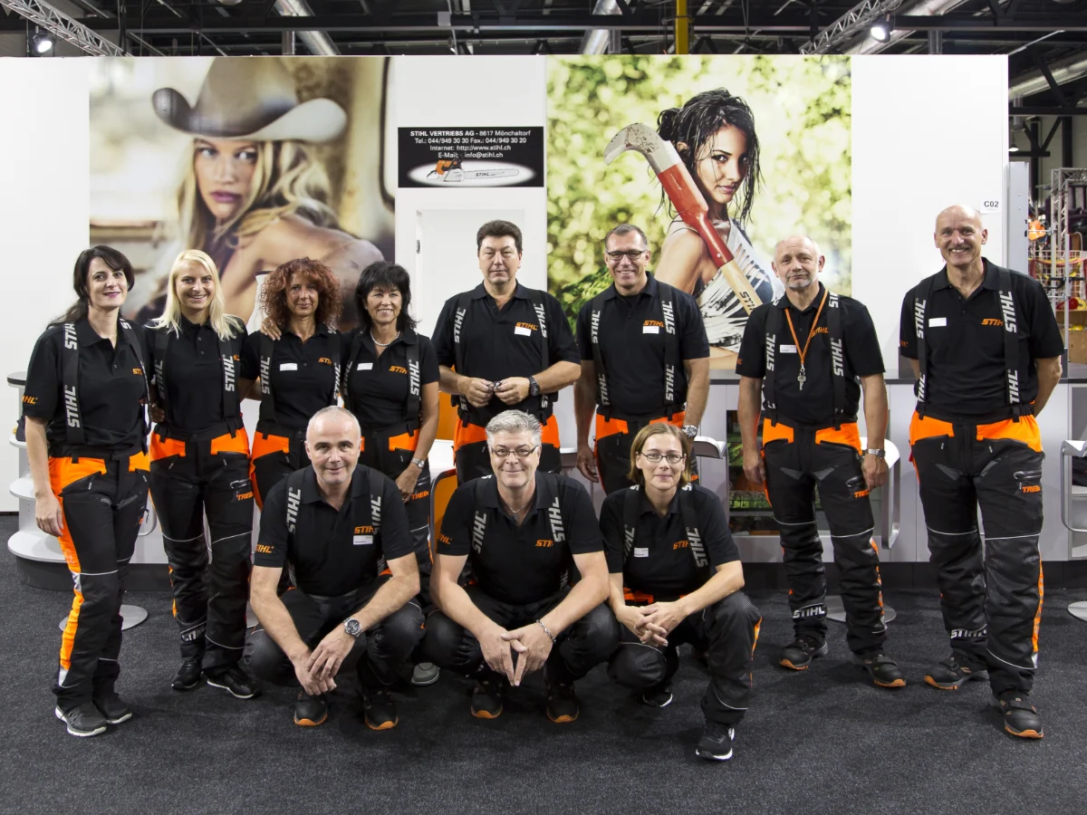 Messe-Team aus Hosts und Hostessen in einheitlicher Kleidung vor einer Branding-Wand, Gruppenfoto in Fußballaufstellung bei Event und Promotion Einsatz