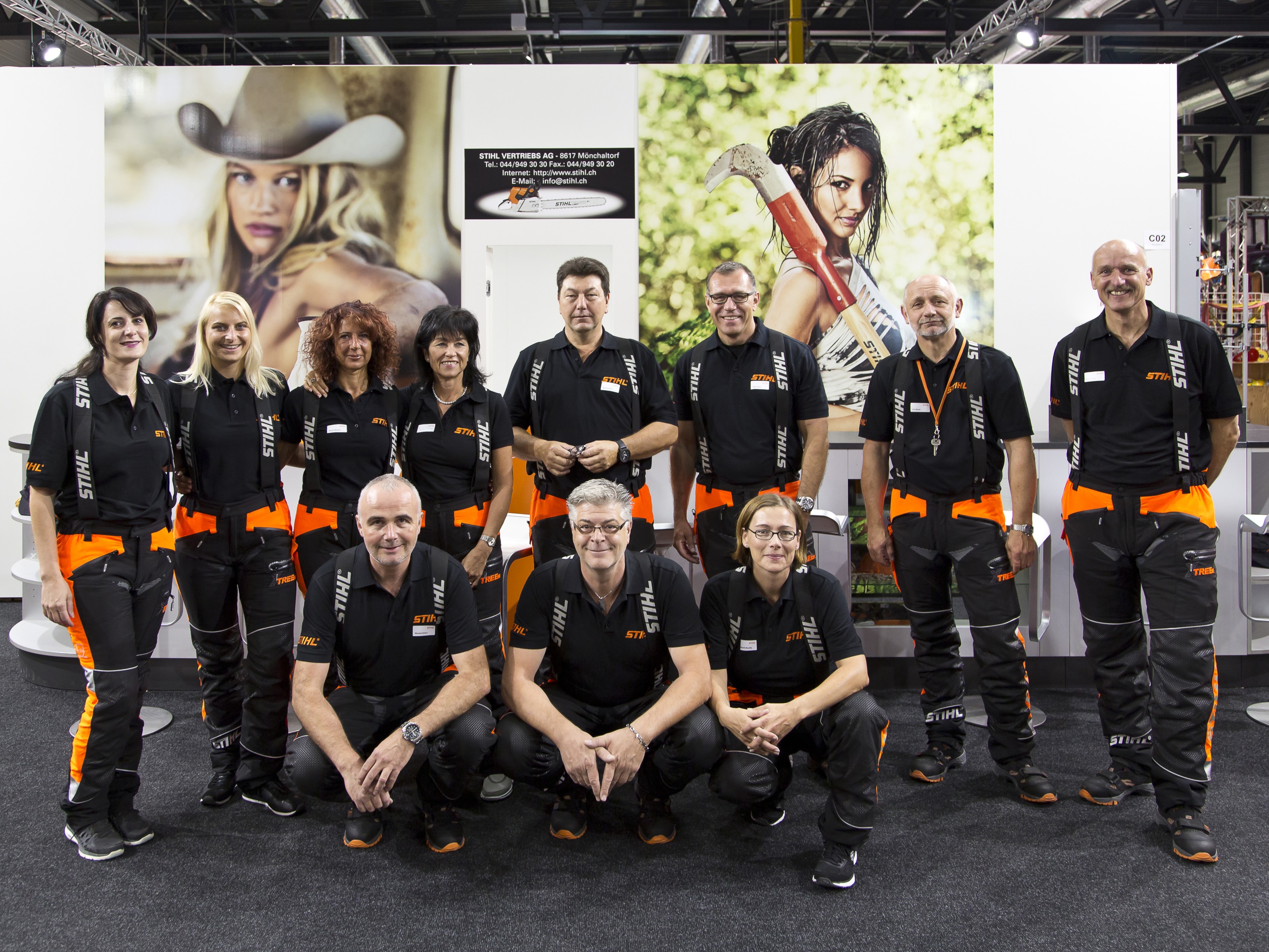 Messe-Team aus Hosts und Hostessen in einheitlicher Kleidung vor einer Branding-Wand, Gruppenfoto in Fußballaufstellung bei Event und Promotion Einsatz