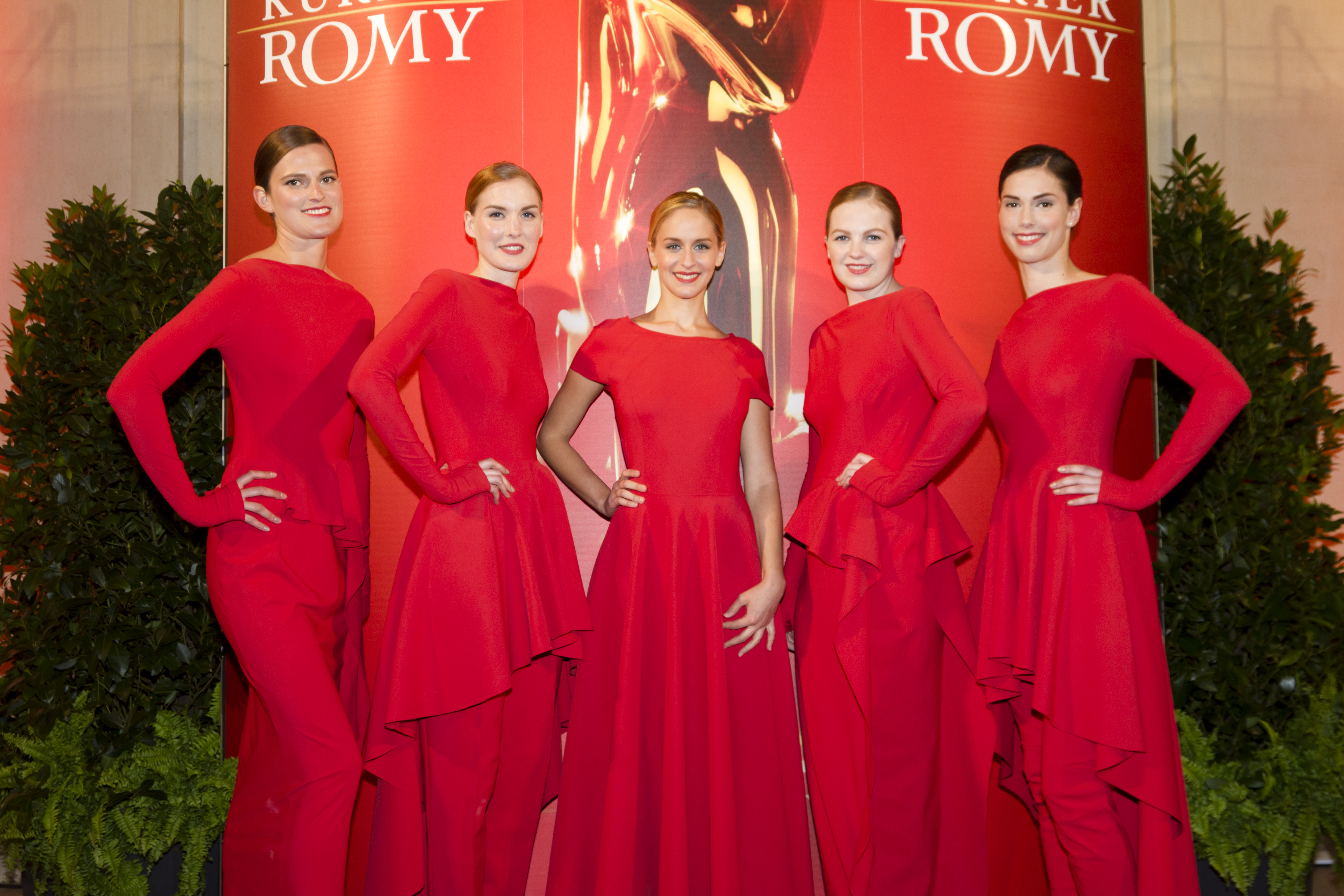 Fünf Modelhostessen in roten Abendkleidern posieren auf dem roten Teppich, eleganter Auftritt mit Lächeln bei Gala, Event und Markenpräsentation