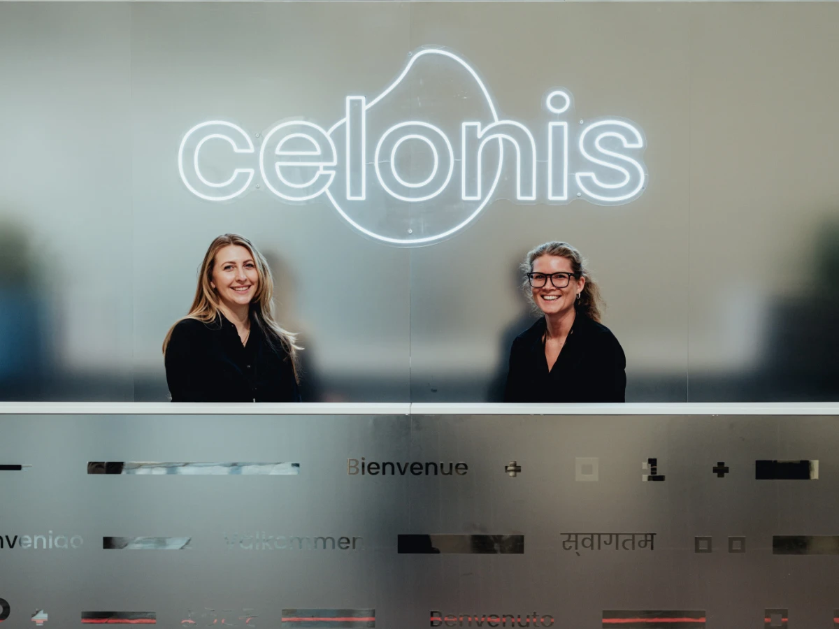 Zwei Hostessen in schwarzen Outfits sitzen hinter einem Messestand mit Markenlogo, freundlicher Empfang und Betreuung bei Messe und Promotion Einsatz