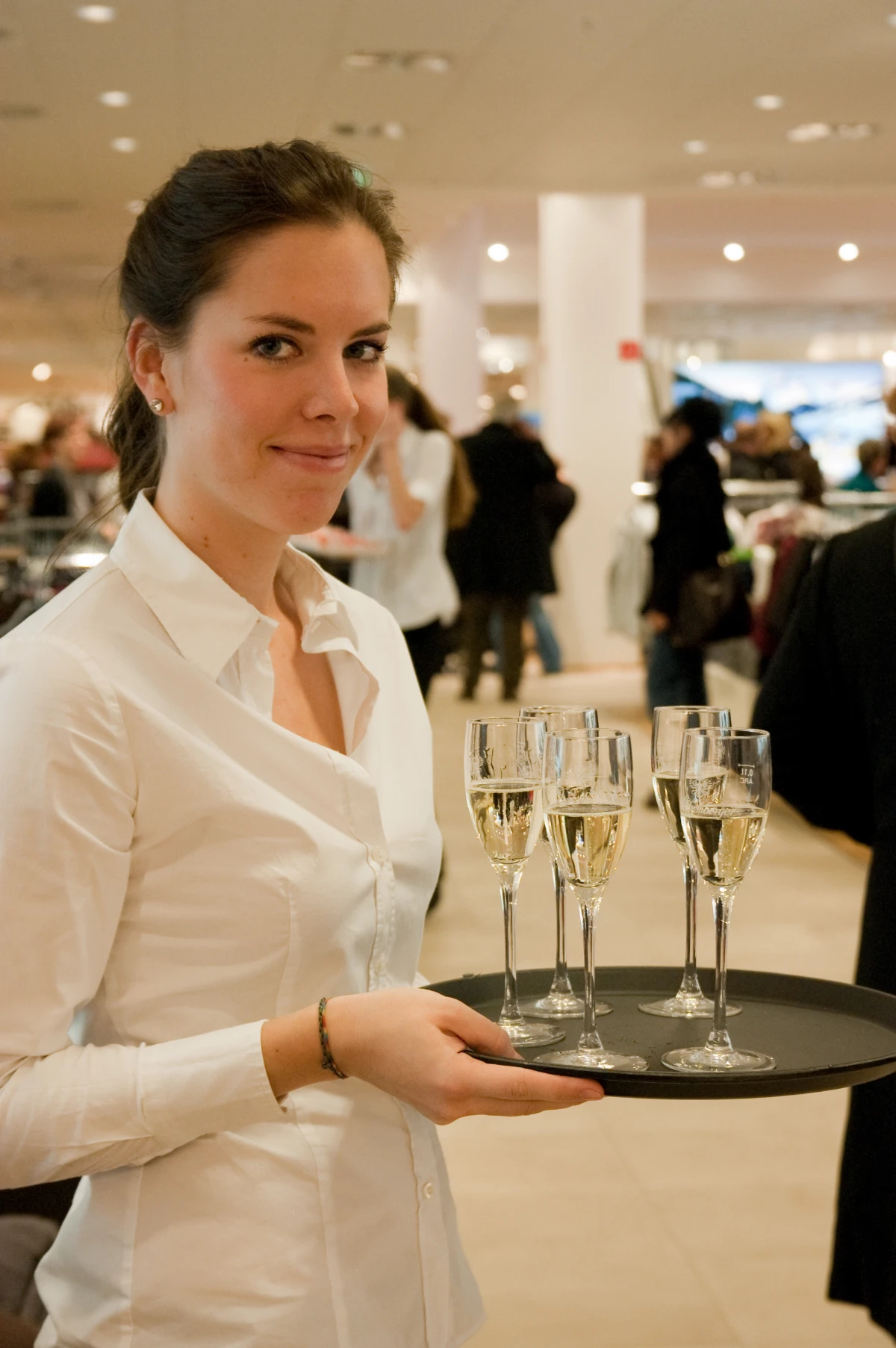 Catering Hostess im weißen Hemd mit Tablet und Gläsern, Haare zusammengebunden, lächelnder Service bei Event, Gala und Veranstaltung