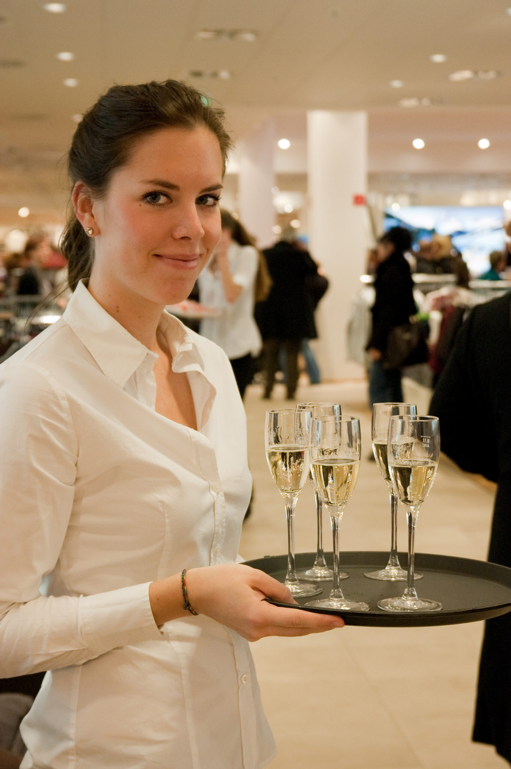 Catering Hostess im weißen Hemd mit Tablet und Gläsern, Haare zusammengebunden, lächelnder Service bei Event, Gala und Veranstaltung