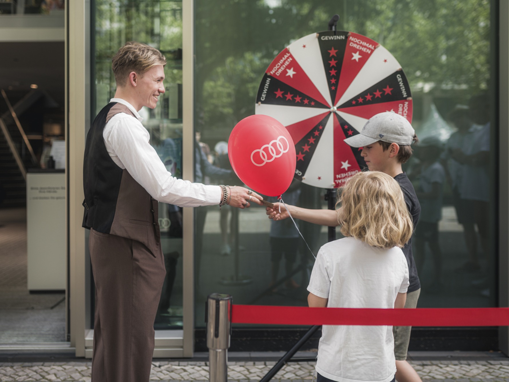 Mann verteilt rote Ballons an Kinder vor einer Drehscheibe, familienfreundliche Promotion Aktion bei Event und Markenaktivierung