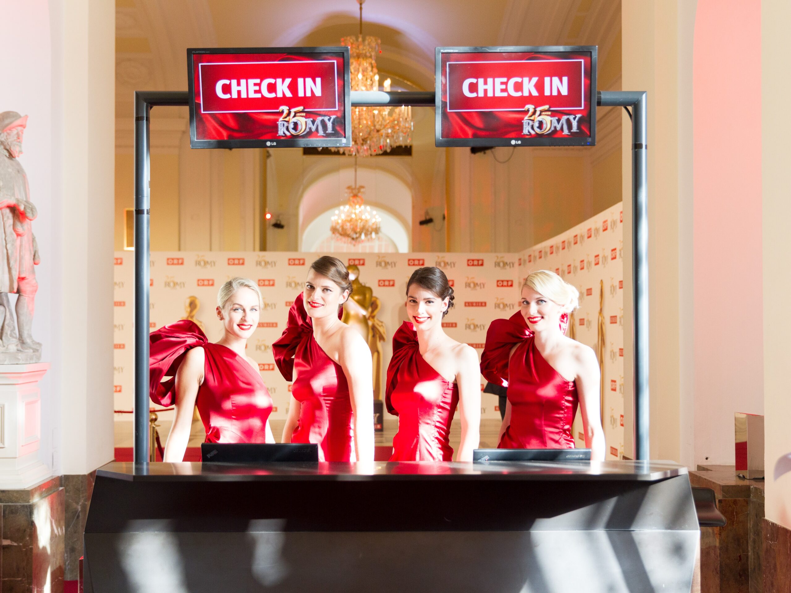 > Vier Hostessen in eleganten roten Abendkleidern an der Akkreditierung, stilvoller Empfang und Check-in bei Event, Gala und Veranstaltung