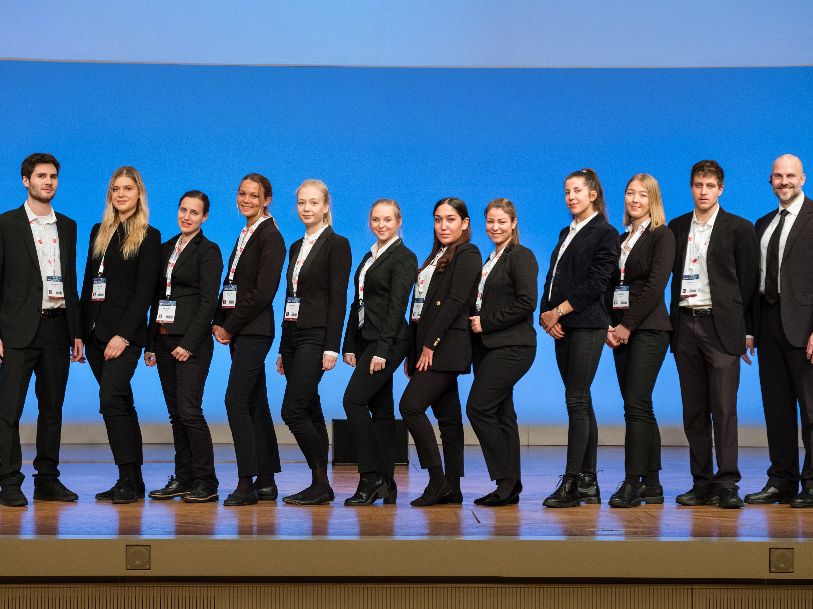 Tagungshost und Hostess im Anzug mit Badge blicken lächelnd in die Kamera, professioneller Empfang und Betreuung bei Konferenz und Event
