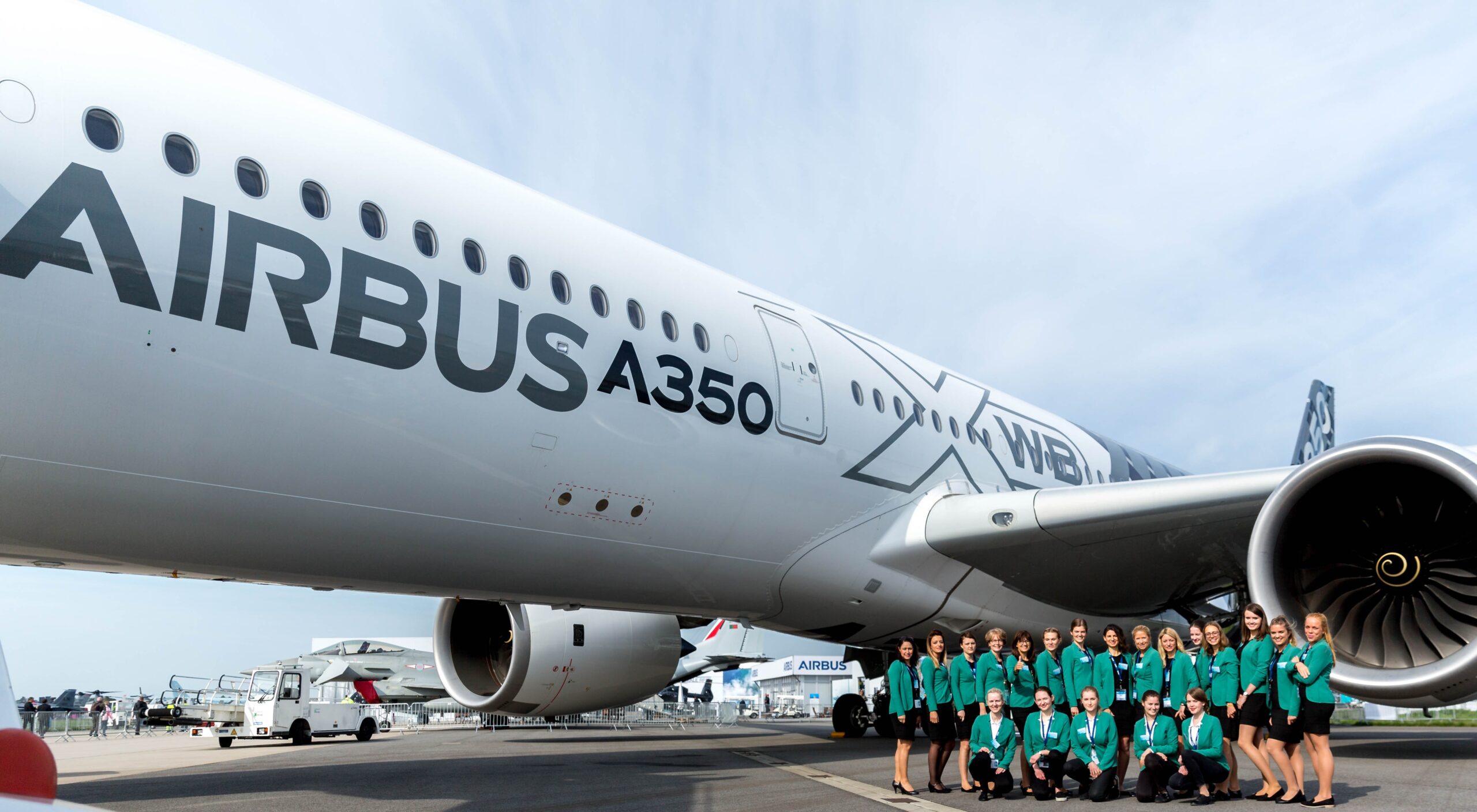 Transferhostessen in grünem Blazer und schwarzem Rock vor einem Flugzeug, lächelnder Empfangsservice bei Event, Messe und Flughafenaktion