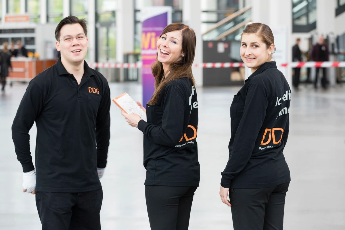 Hosts und Hostessen in einheitlichen Outfits blicken lächelnd über die Schulter in die Kamera, positive Stimmung bei Messe, Promotion und Eventeinsatz