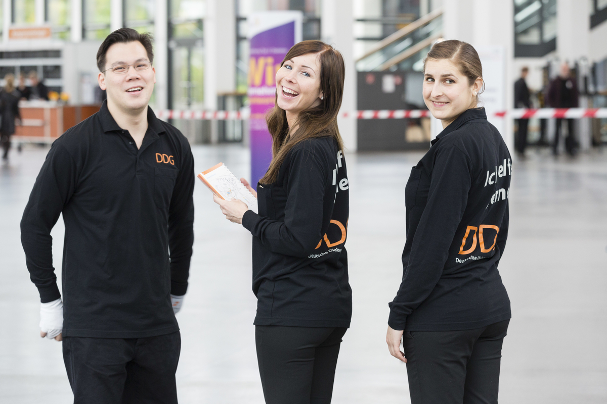 Hosts und Hostessen in einheitlichen Outfits blicken lächelnd über die Schulter in die Kamera, positive Stimmung bei Messe, Promotion und Eventeinsatz