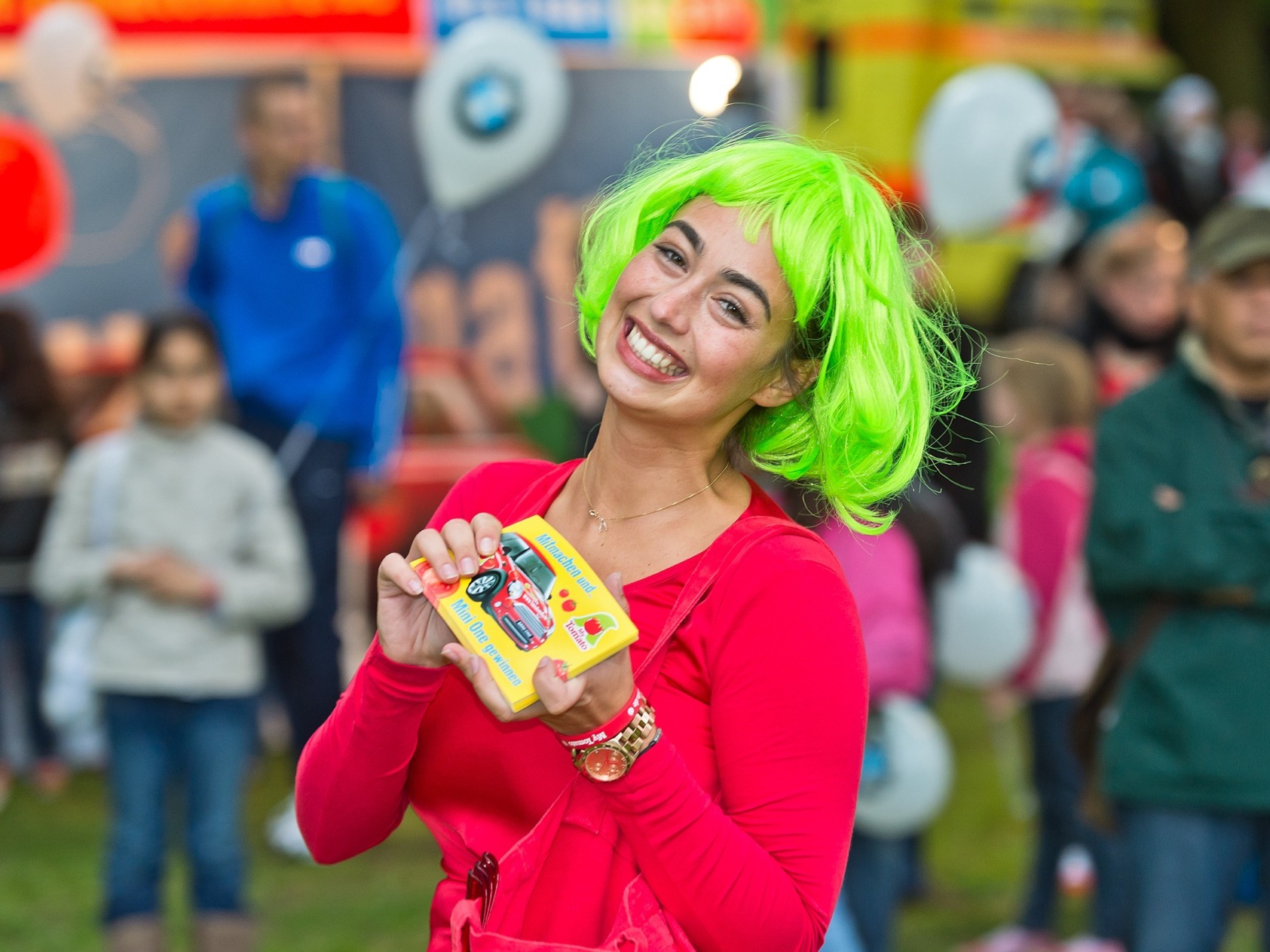 Promotion Hostess mit grüner Perücke und roter Kleidung hält Flyer in der Hand, lächelnder Einsatz bei Event, Messe und Markenaktion