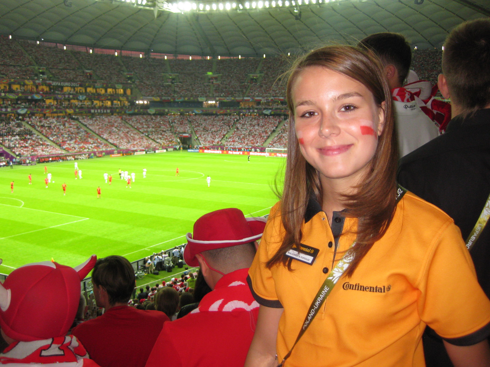 hostess im orangenen Oberteil lächelt im Stadion in die Kamera, Promotion Einsatz bei WM, Event und Markenaktivierung als zimtie