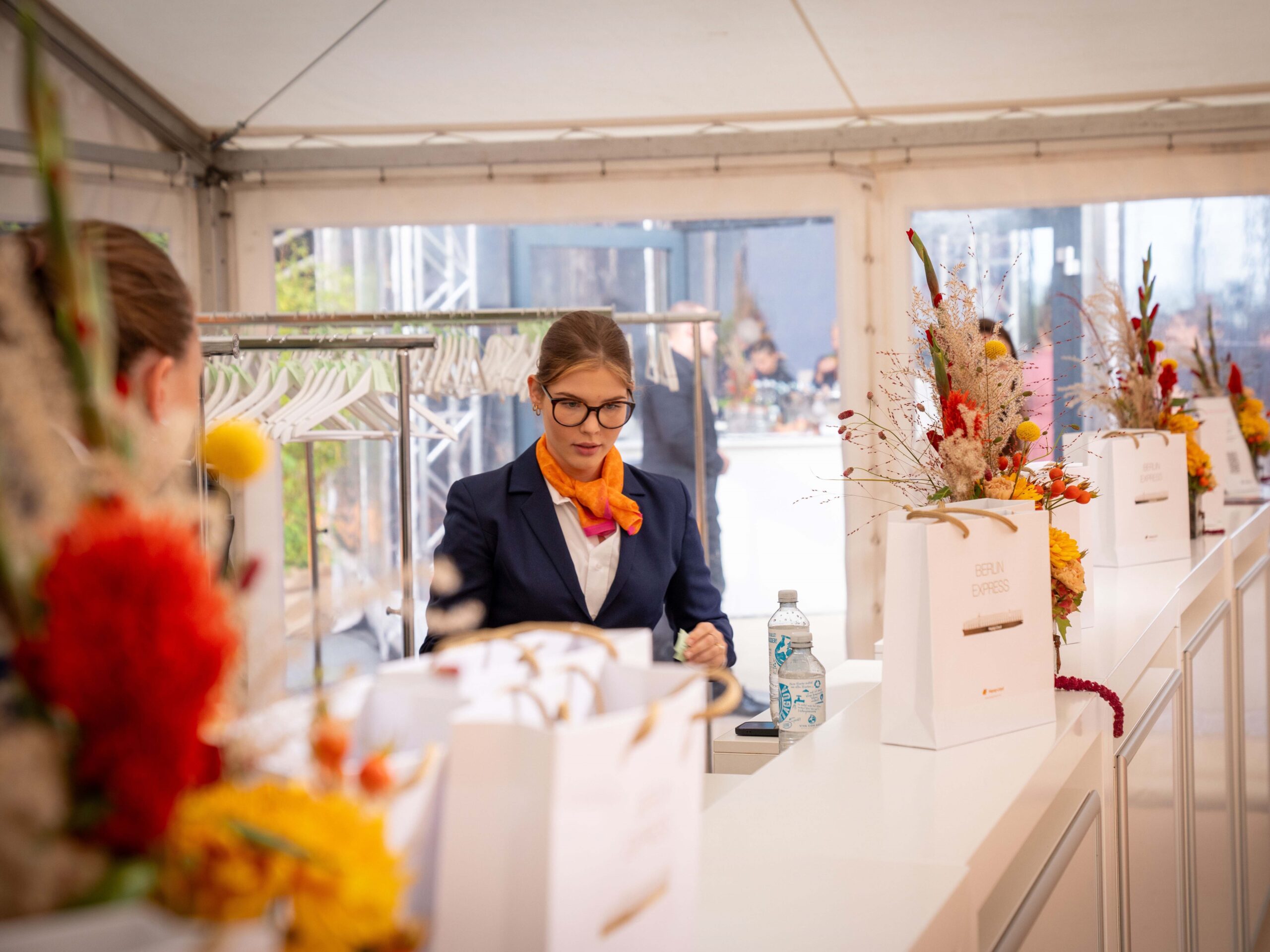 Transferhostess im blauen Hosenanzug mit buntem Halstuch arbeitet an der Garderobe, professioneller Empfangs- und Gästeservice bei Event