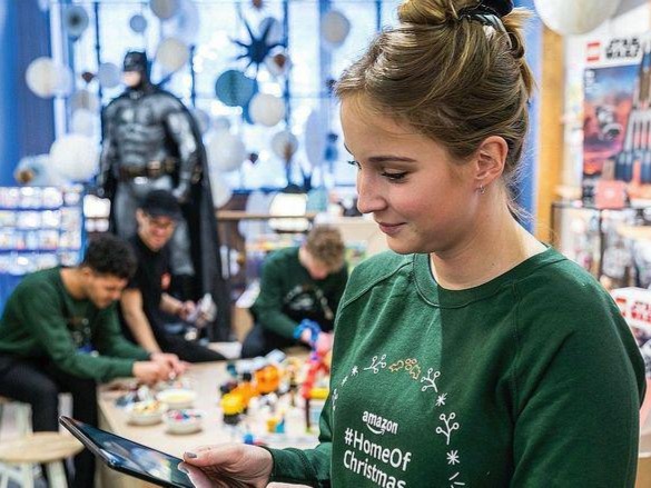 Frau im gr&uuml;nen Pullover mit Dutt blickt auf ein Tablet, im Hintergrund unscharfe M&auml;nner, konzentrierte Arbeitsszene bei Event und Organisation