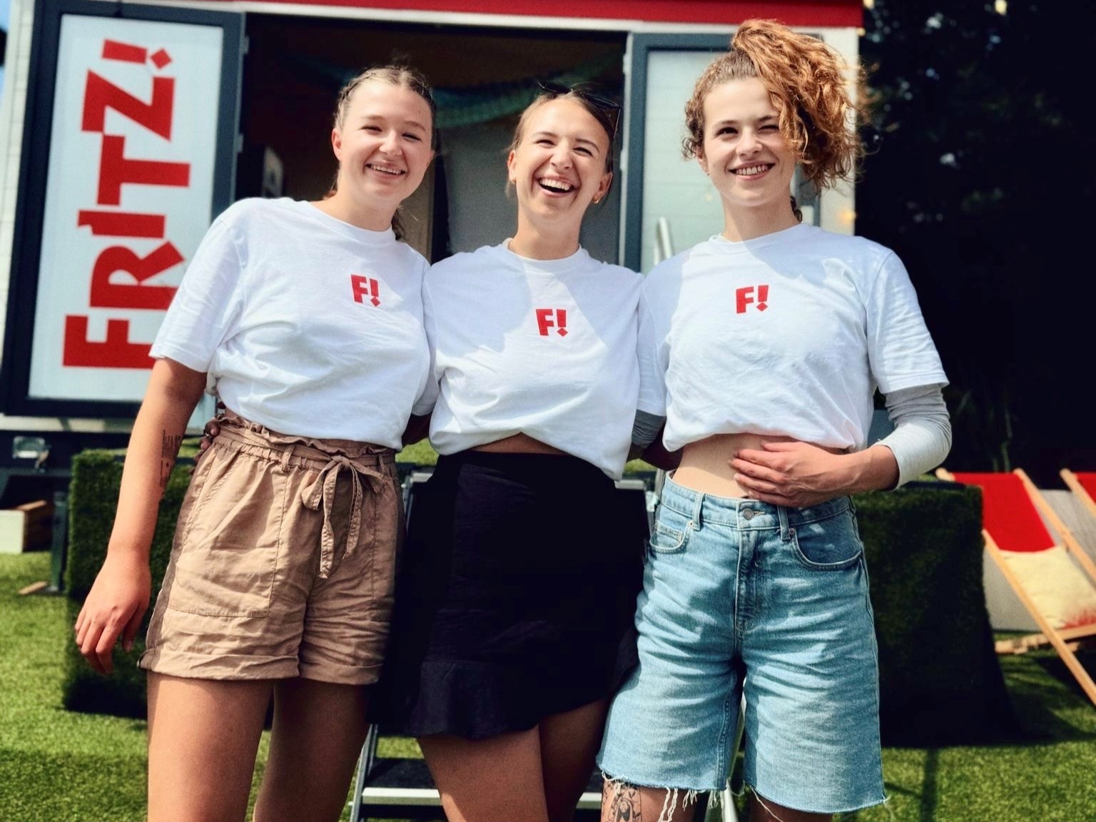 Drei Hostessen in Kassel mit weißen FRITZ! T-Shirts und kurzen Hosen, lächelnder Promotion Einsatz für cinnamon bei Event und Markenaktion