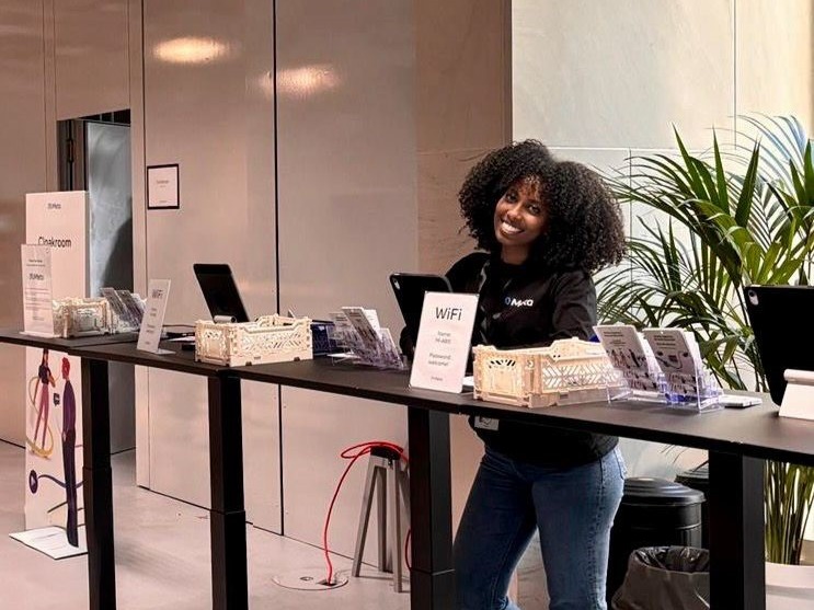 Hostess in Blue Jeans und schwarzem T-Shirt hinter einem Tresen an der Akkreditierung, lächelnder Empfangsservice bei Event und Messe.