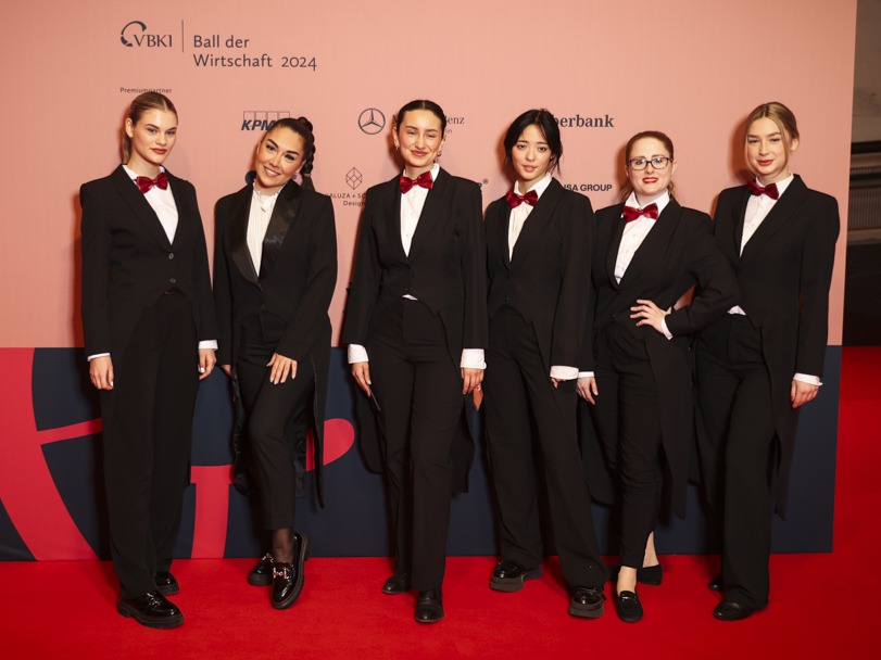 Hostessen im schwarzen Hosenanzug mit weißem Hemd und roter Fliege vor einer Fotowand, eleganter Empfangsservice bei Gala, Event und Markenpräsentation