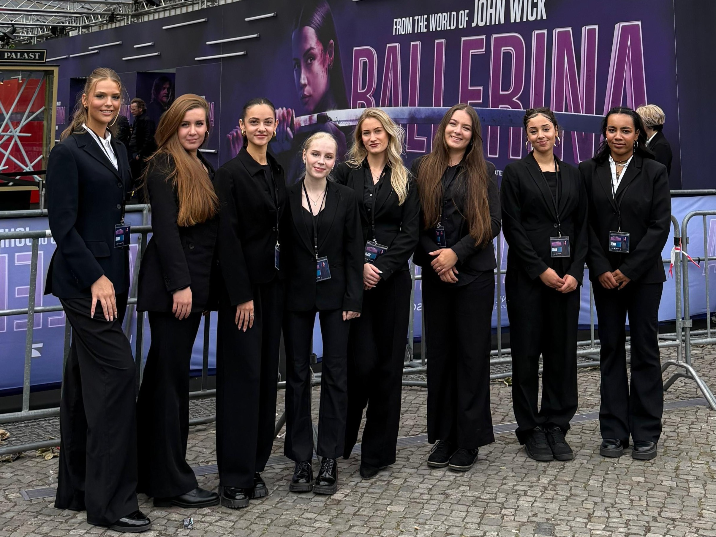 Hostessen im schicken Hosenanzug mit schwarzer Anzugshose und weißem Hemd vor einer Fotowand einer Filmpremiere, professioneller Empfang bei Event und Gala.