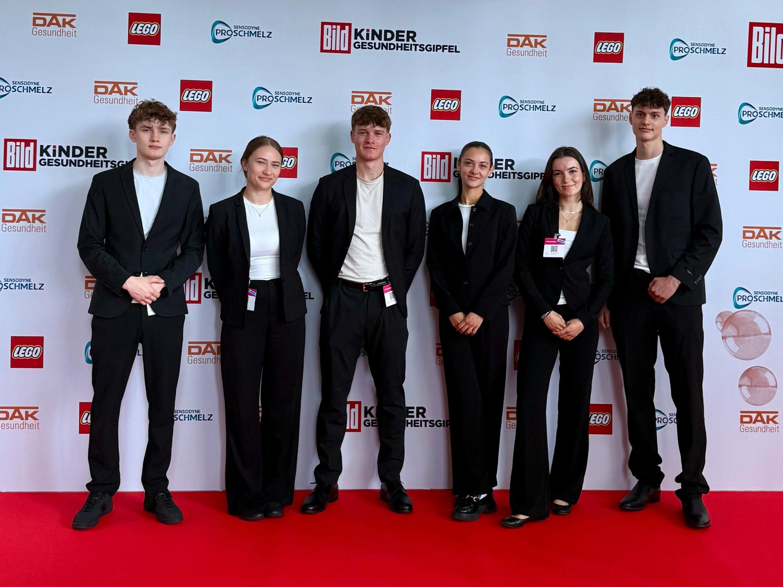 Hosts und Hostessen in eleganten Anzügen vor einer Fotowand auf dem roten Teppich, stilvoller Empfangsservice und professioneller Gala-Auftritt bei cinnamon Events