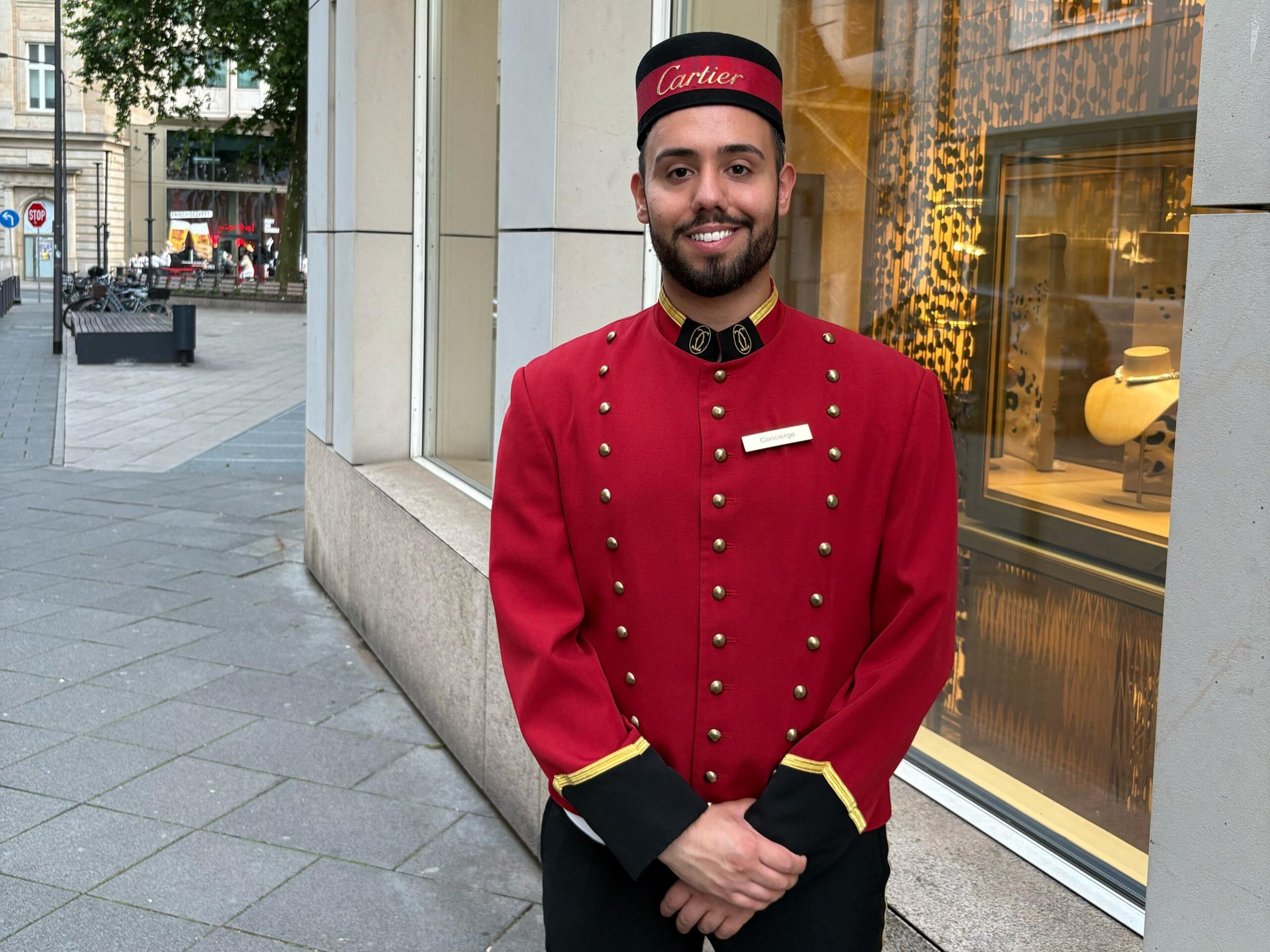 Cartier Page in rot-schwarz-goldenem Outfit mit Hut vor dem Cartier Store in Berlin, eleganter Empfangsservice bei Luxus-Event und Markenpräsentation