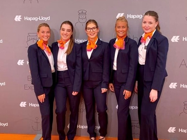 Hostessen in eleganten blauen Anzügen mit orangenen Halstüchern auf dem roten Teppich vor einer Fotowand, professioneller Gala- und Empfangsservice von cinnamon