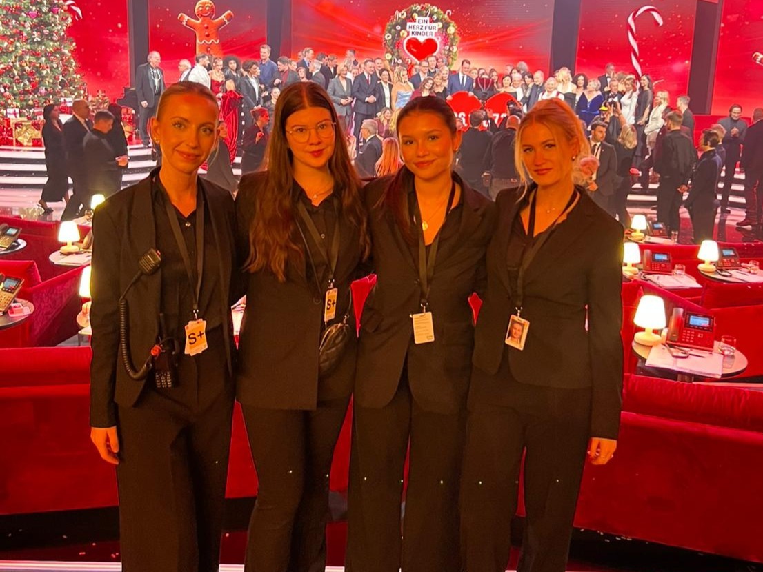 Vier Hostessen in schwarzen Anzügen vor einer Bühne bei „Ein Herz für Kinder“, eleganter Empfangsservice und professioneller Gala-Auftritt von cinnamon
