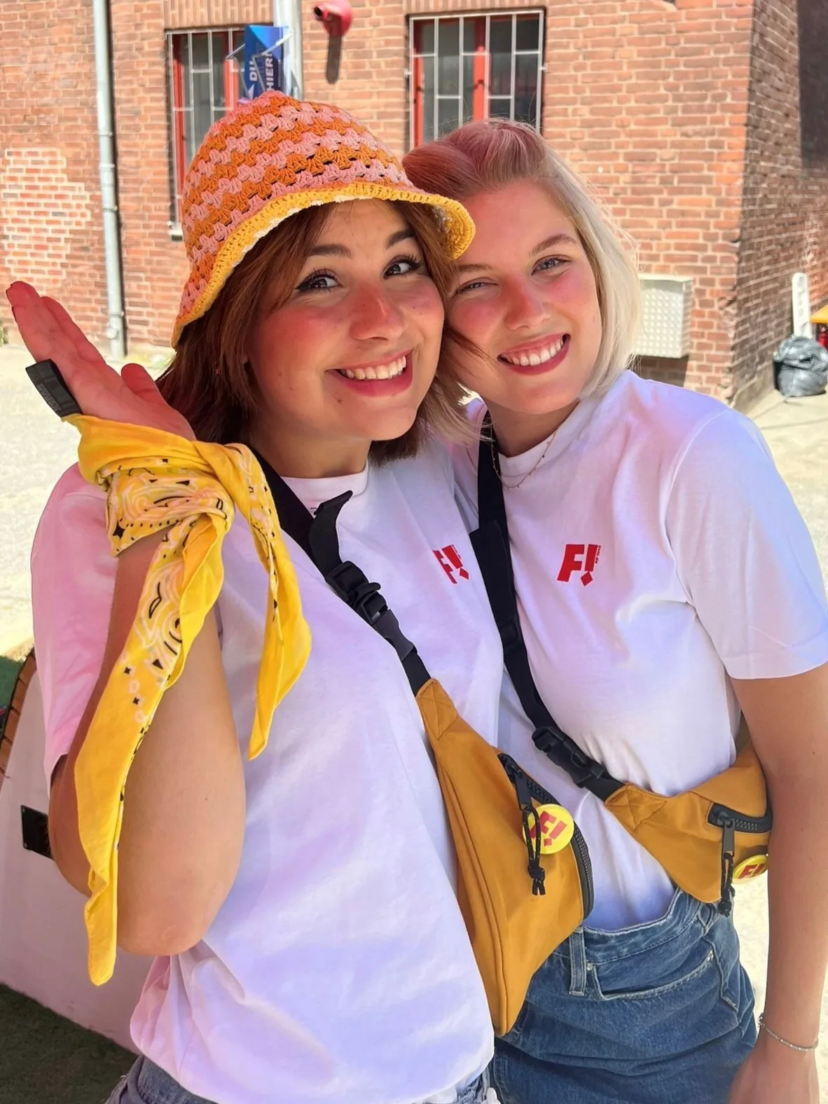 Zwei Promoterinnen mit weißen T-Shirts, Bucket Hats und gelben Accessoires lächeln glücklich in die Kamera, sommerliche Promotion Aktion von cinnamon bei Event und Markenaktivierung