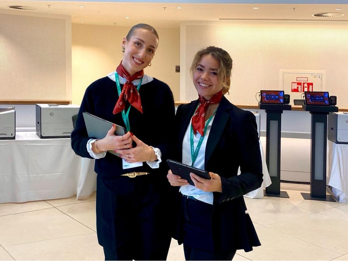 Zwei Hostessen in schicken Anzügen mit Tablets in der Hand lächeln fröhlich in die Kamera, professioneller Empfangs- und Eventservice bei cinnamon