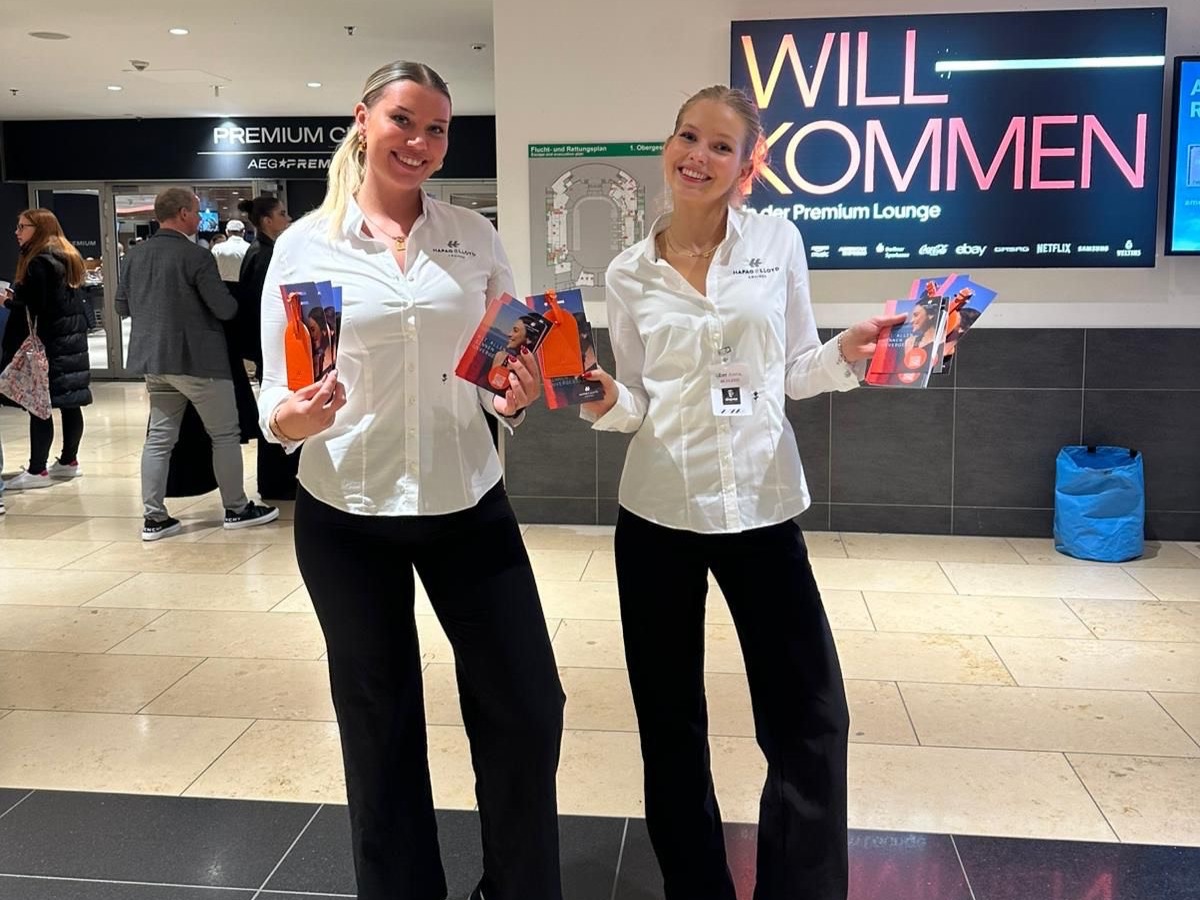 Zwei Hostessen in weißen Blusen und schwarzen Anzugshosen halten Flyer in der Hand, lächelnder Promotion- und Empfangsservice bei Event und Messe