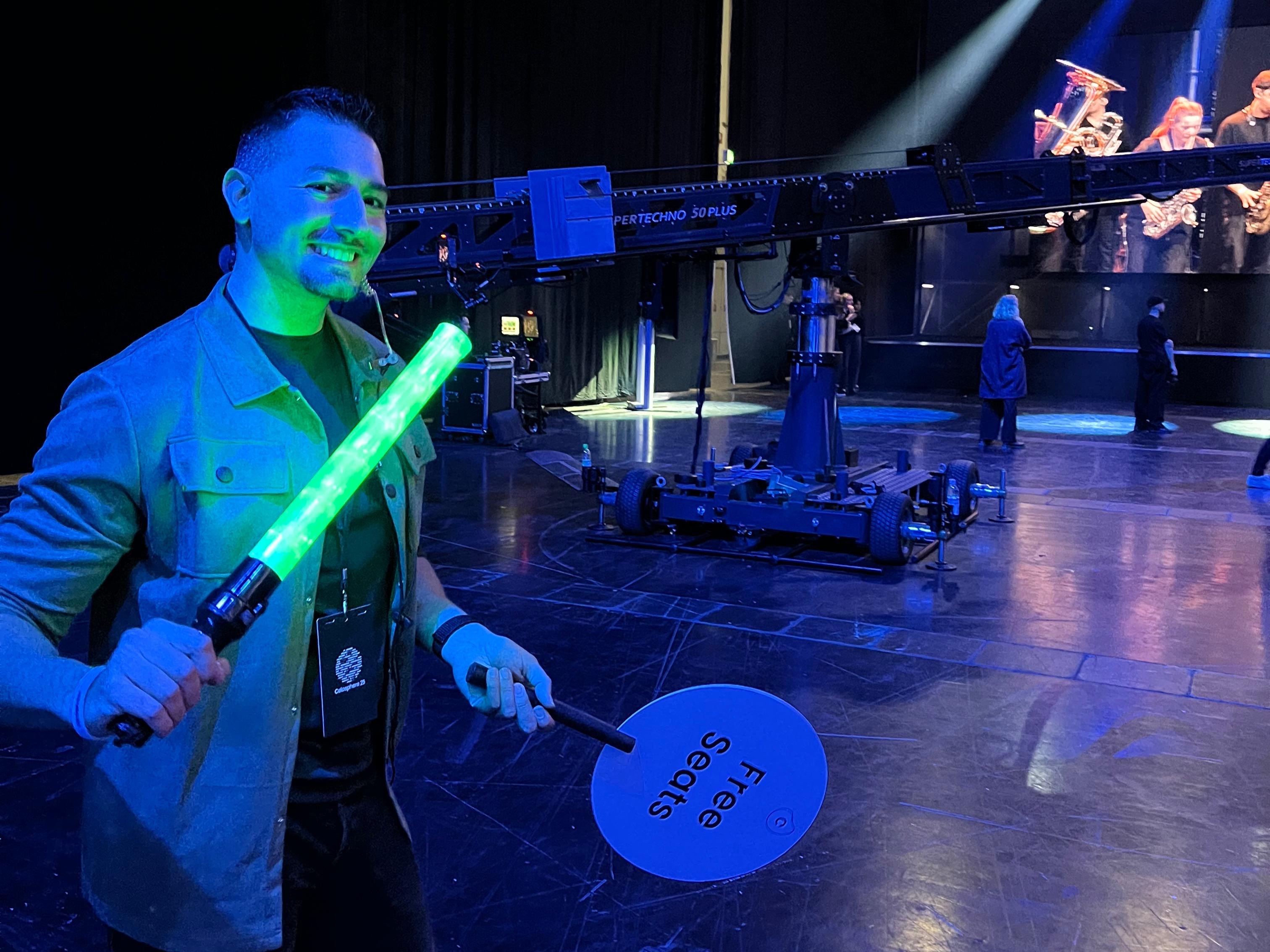 Host mit leuchtendem Stab und Wegweiser-Schild im Backstage-Bereich lächelt in die Kamera, professioneller Wegeleitungs- und Eventservice bei Veranstaltung und Show